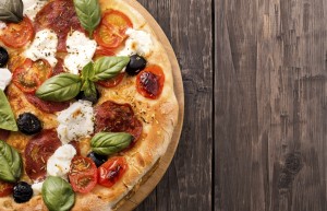 Rustic pizza with salami, mozzarella, olives and basil on wooden
